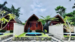 A row of wooden cabins with a stone pathway leading to a central circular water feature. - Green Lake Bali (Kintamani)