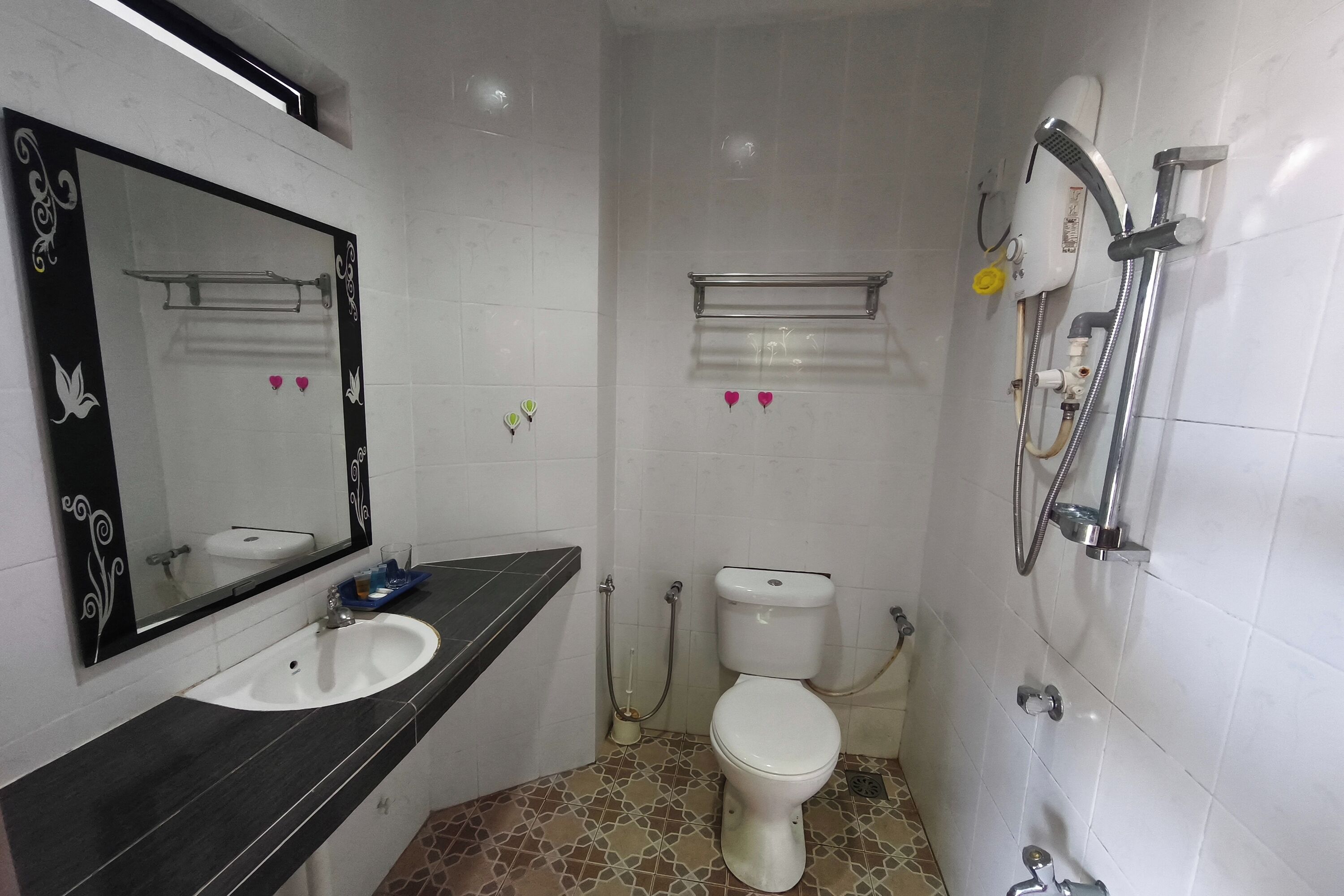 A bathroom with a white toilet, a sink with a black countertop, a mirror with decorative frames, and a shower area with a handheld showerhead.