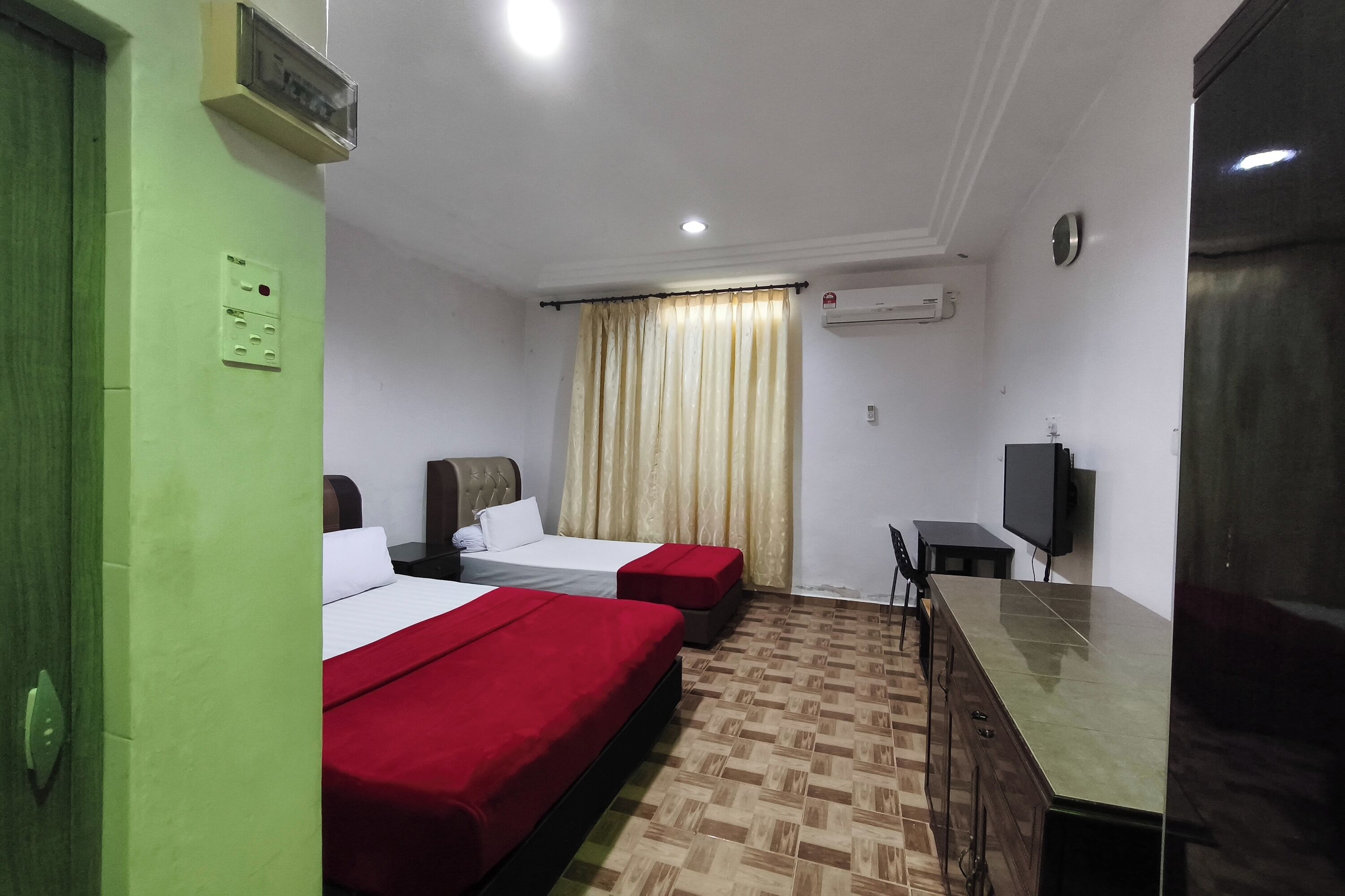 A hotel room with two beds, a desk, a chair, a television, and an air conditioning unit.