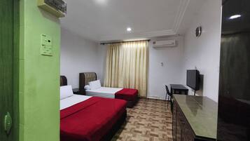 A hotel room with two beds, a desk, a chair, a television, and an air conditioning unit.