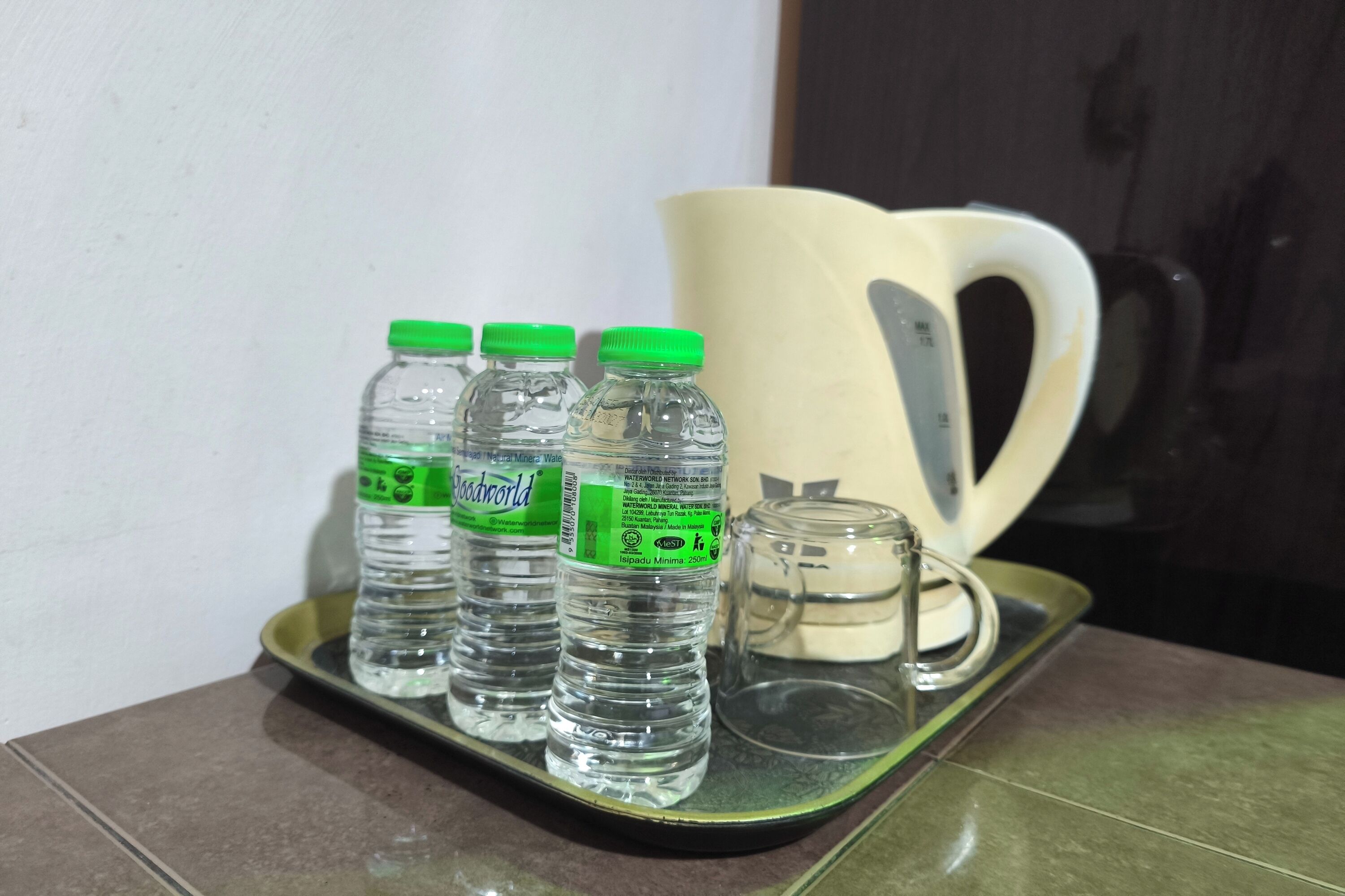 Una bandeja con tres botellas de agua y una taza de cerámica sobre una superficie de baldosas.