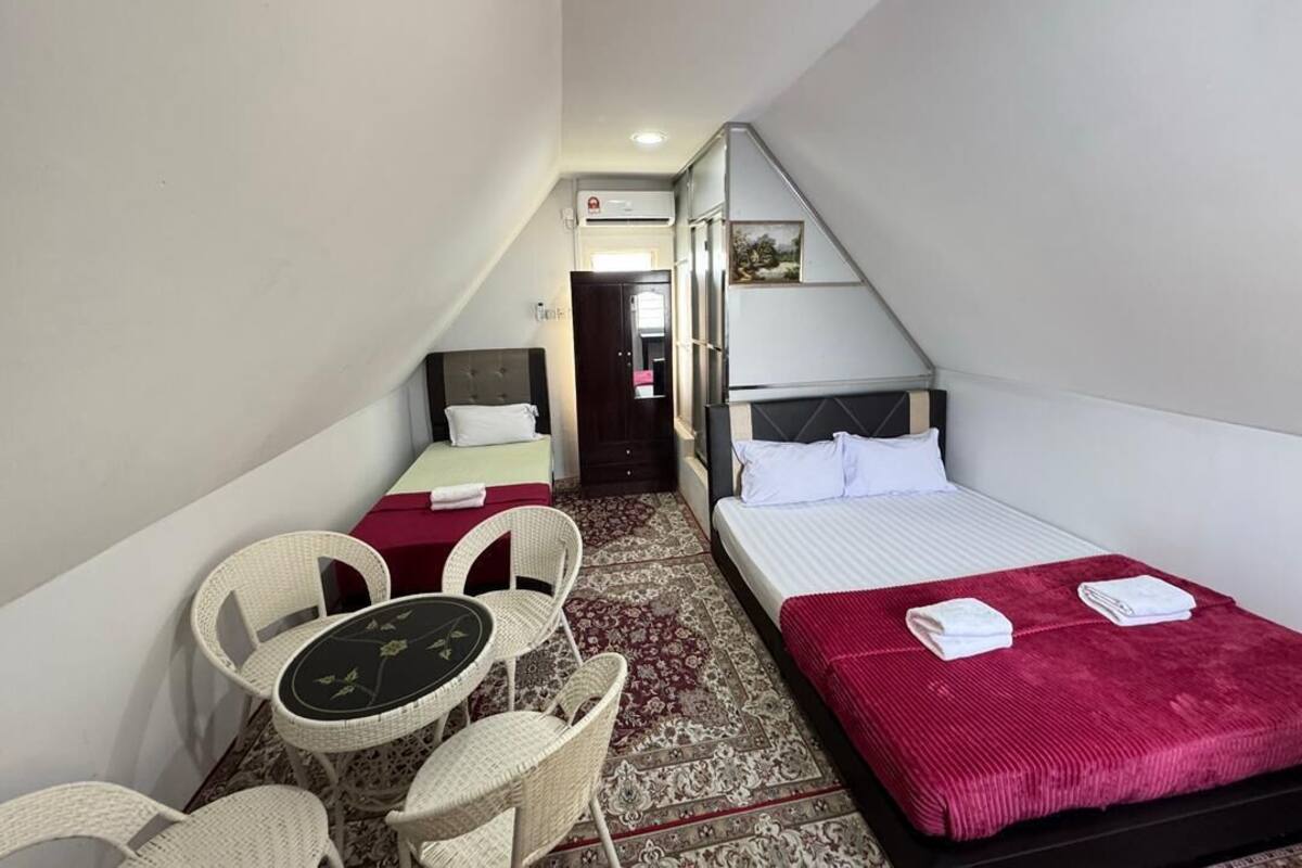 A small, triangular room with two beds, a small table with chairs, and a red carpet.