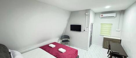 Una habitación pequeña y bien iluminada con una cama, un escritorio y un televisor.