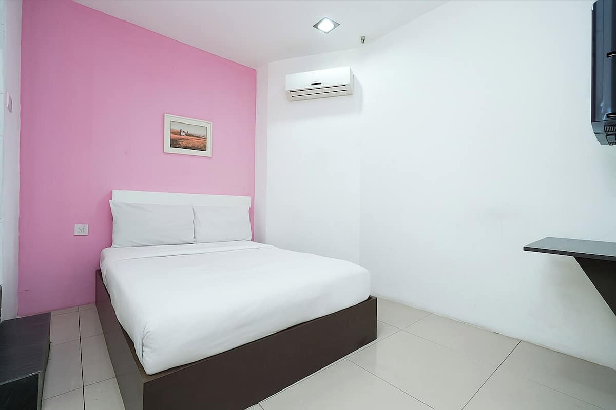 A bedroom with a bed, a pink wall, a white wall, an air conditioning unit, and a small shelf.