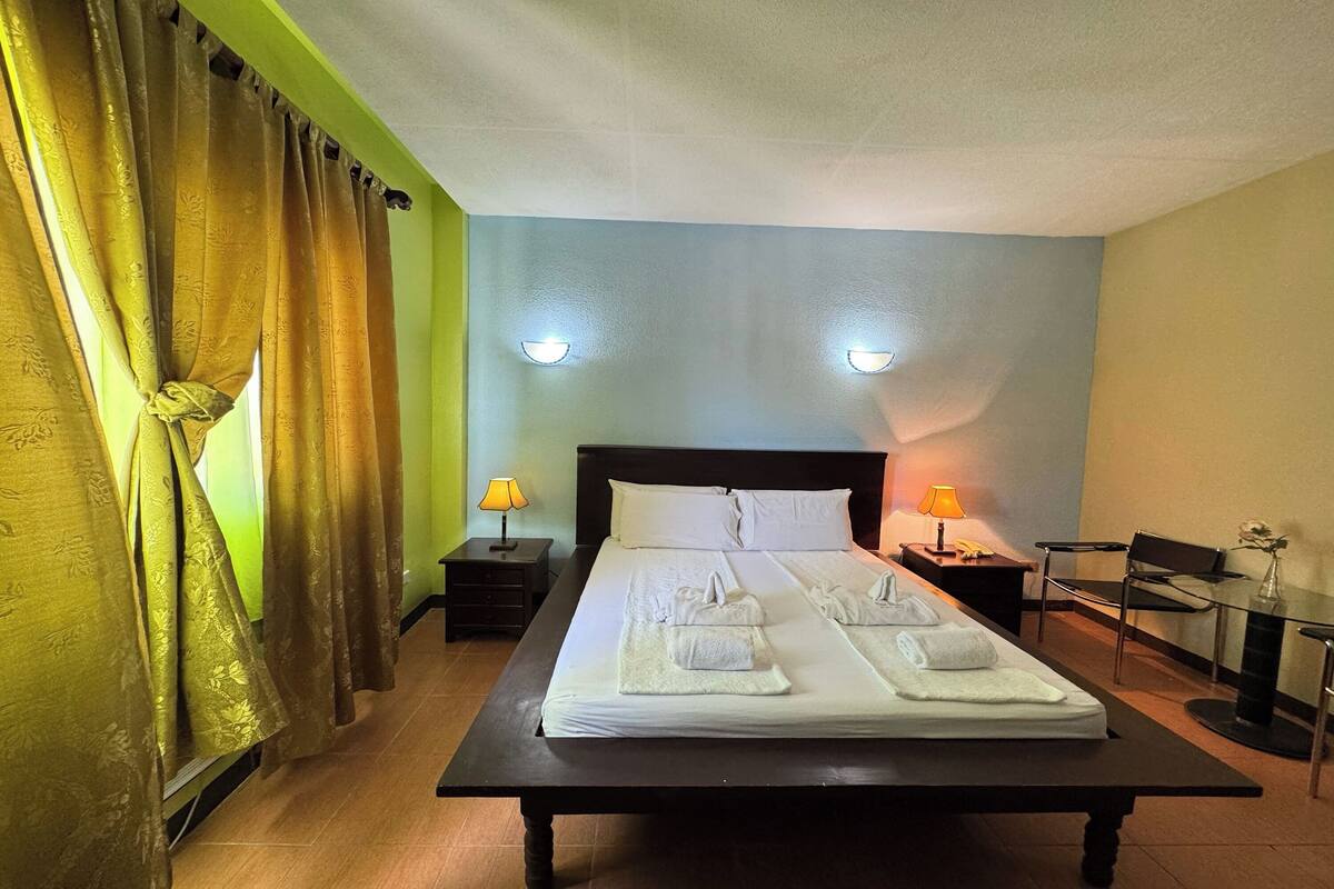 Ein ordentlich bezogenes Bett mit Handtüchern, ein Nachttisch mit Lampe und ein Sessel in einem Hotelzimmer.