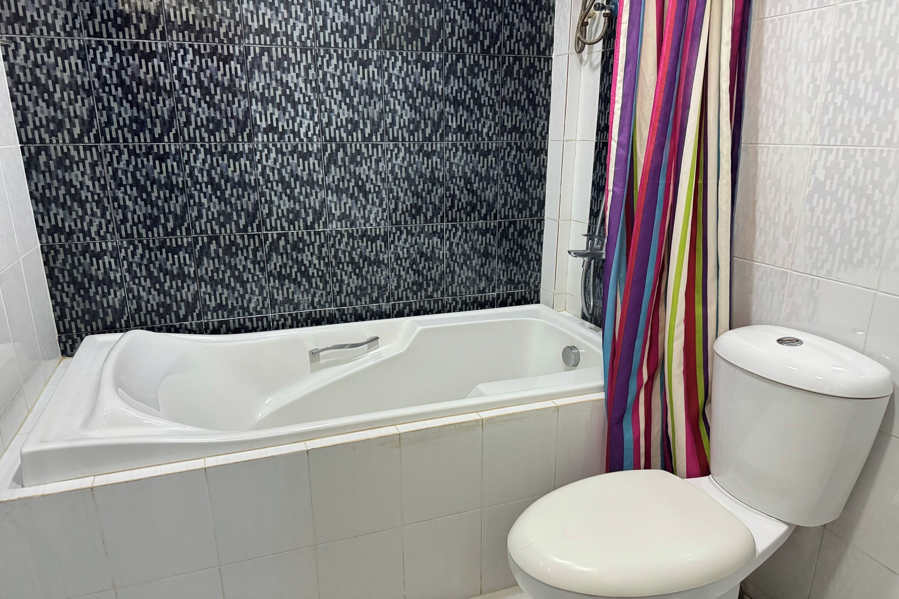 Un baño con una bañera blanca, un inodoro blanco y una cortina de ducha con rayas multicolores.
