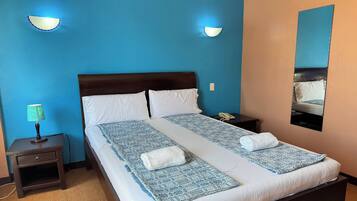 Een net opgemaakt bed met witte lakens en blauw gestreepte bedspreien, een bedlampje en een nachtkastje met een lade.