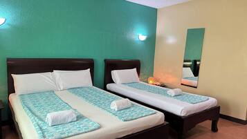 Dos camas individuales con ropa blanca y colchas estampadas en tonos turquesa, una pared verde y un espejo en la pared contigua.