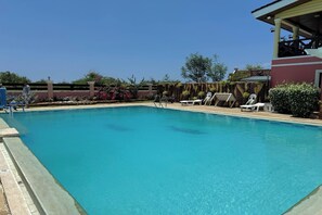 A swimming pool with lounge chairs and a covered area.