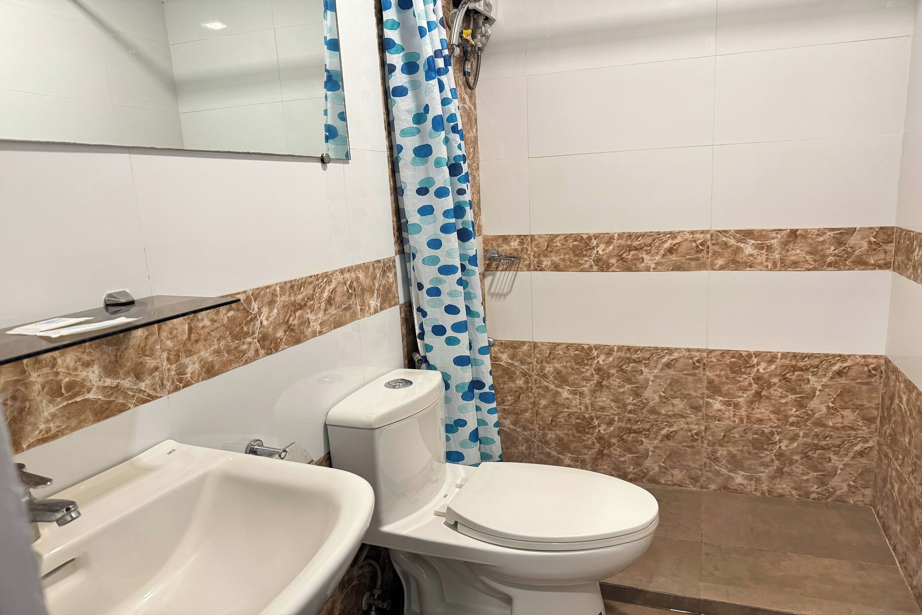 Une salle de bain avec un lavabo blanc, des toilettes et un rideau de douche à pois bleus.