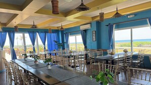 A spacious dining area with high tables and chairs, large windows with blue curtains, and hanging wicker lamps.