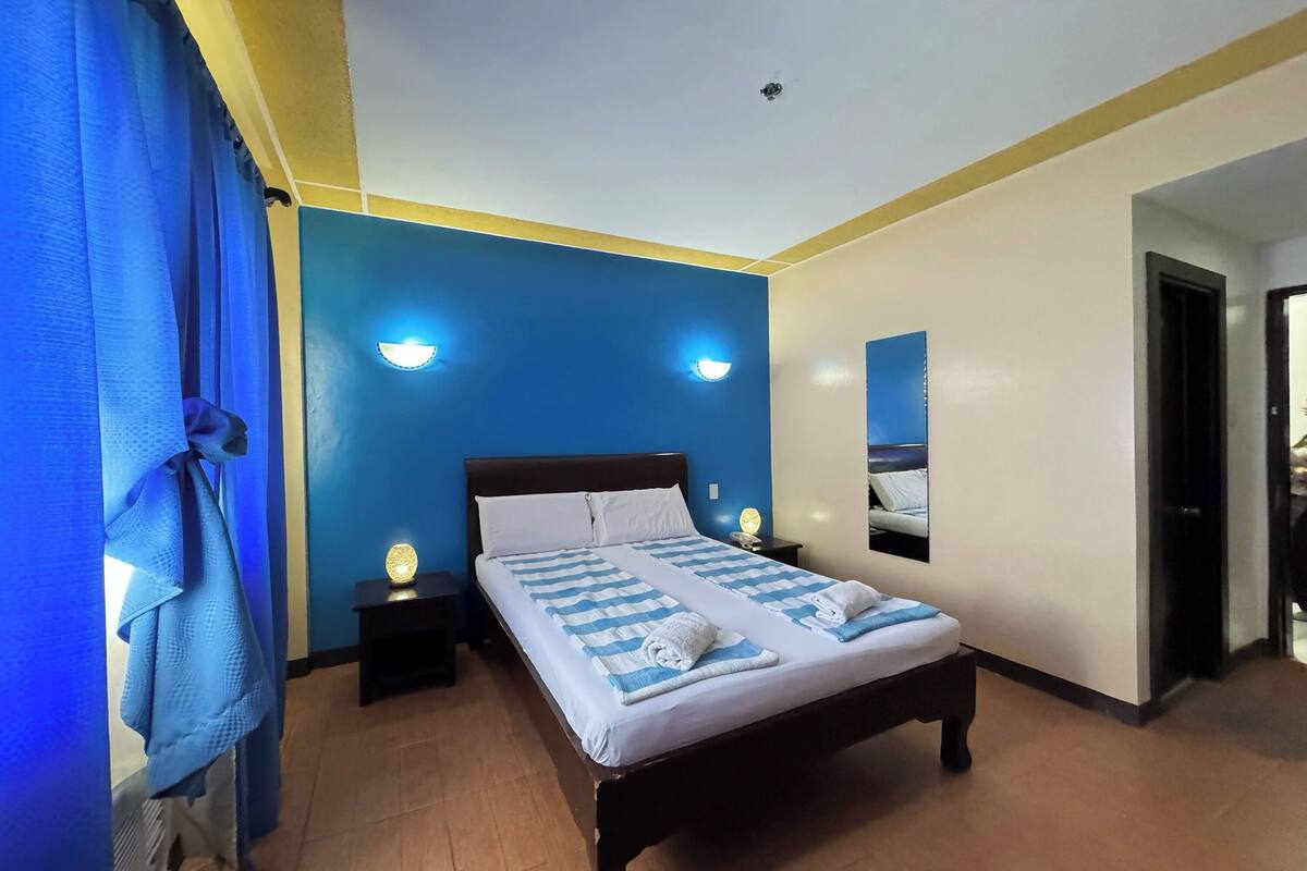 Ein Doppelbett mit blau-weiß gestreifter Bettdecke, zwei Nachttischlampen und einem an der Wand befestigten Spiegel.