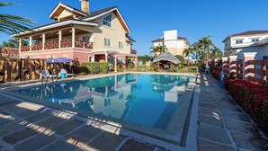 A swimming pool with lounge chairs and a covered area, surrounded by buildings with balconies and a clear blue sky.