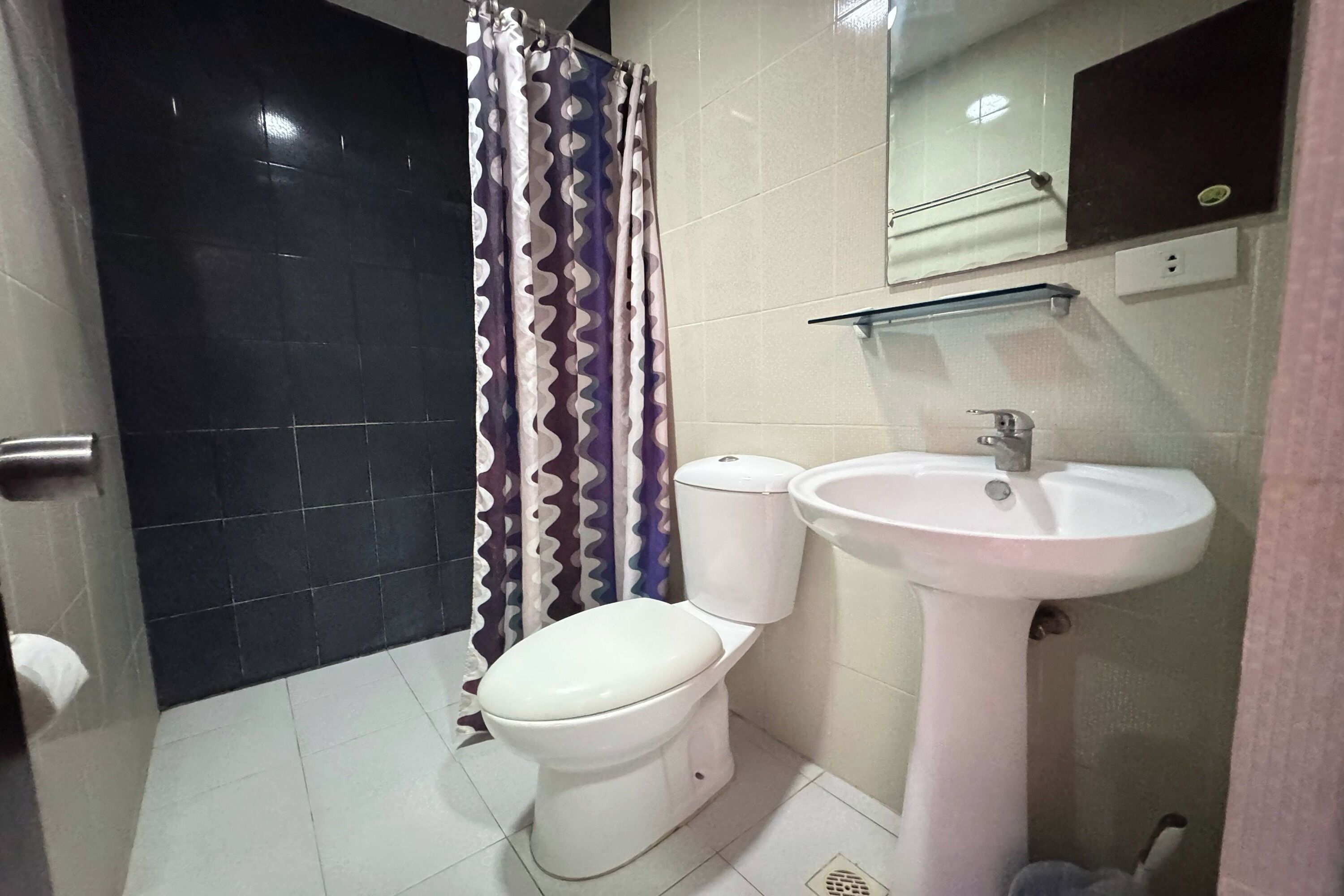 Un baño con inodoro y lavamanos blancos, y una cortina de ducha con estampado en zigzag.