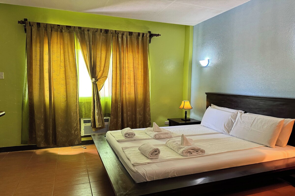 Una habitación de hotel con cama, cortinas, una mesita de noche y una lámpara.