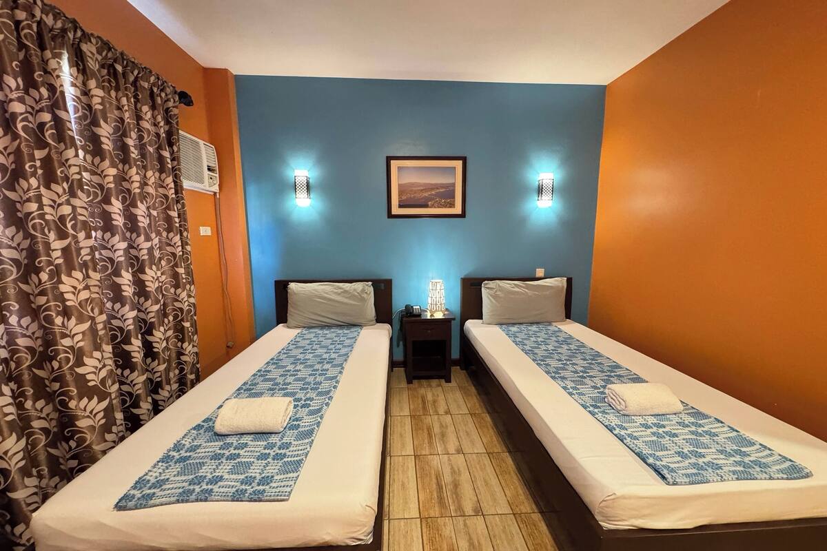 Ein Zimmer mit zwei Betten, einem Nachttisch, einem Bild an der Wand und einem Vorhang.