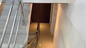 A modern staircase with glass railings and a wooden finish, leading to a room with a dark wooden wall and a white door. - White-Beach Hideaway Resort Puerto Galera (Puerto Galera)