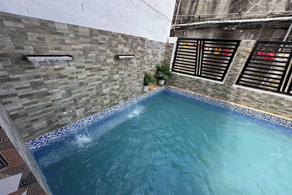 A swimming pool with a tiled edge, a water feature, and a potted plant.