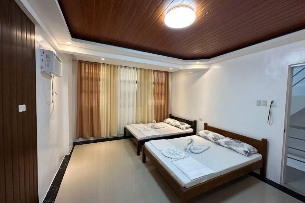 Habitación de hotel con dos camas, techo de madera y un ventanal grande con cortinas.