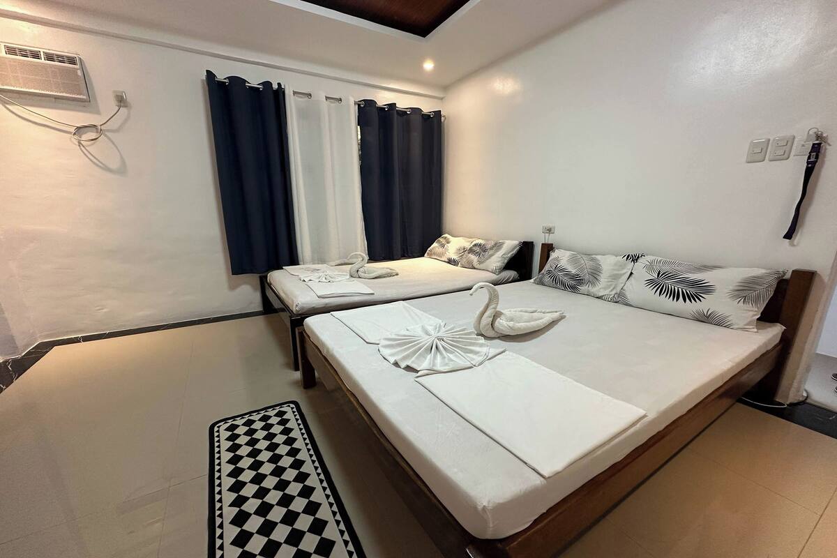 Une chambre d’hôtel avec deux lits, un tapis à carreaux et un ventilateur de plafond.