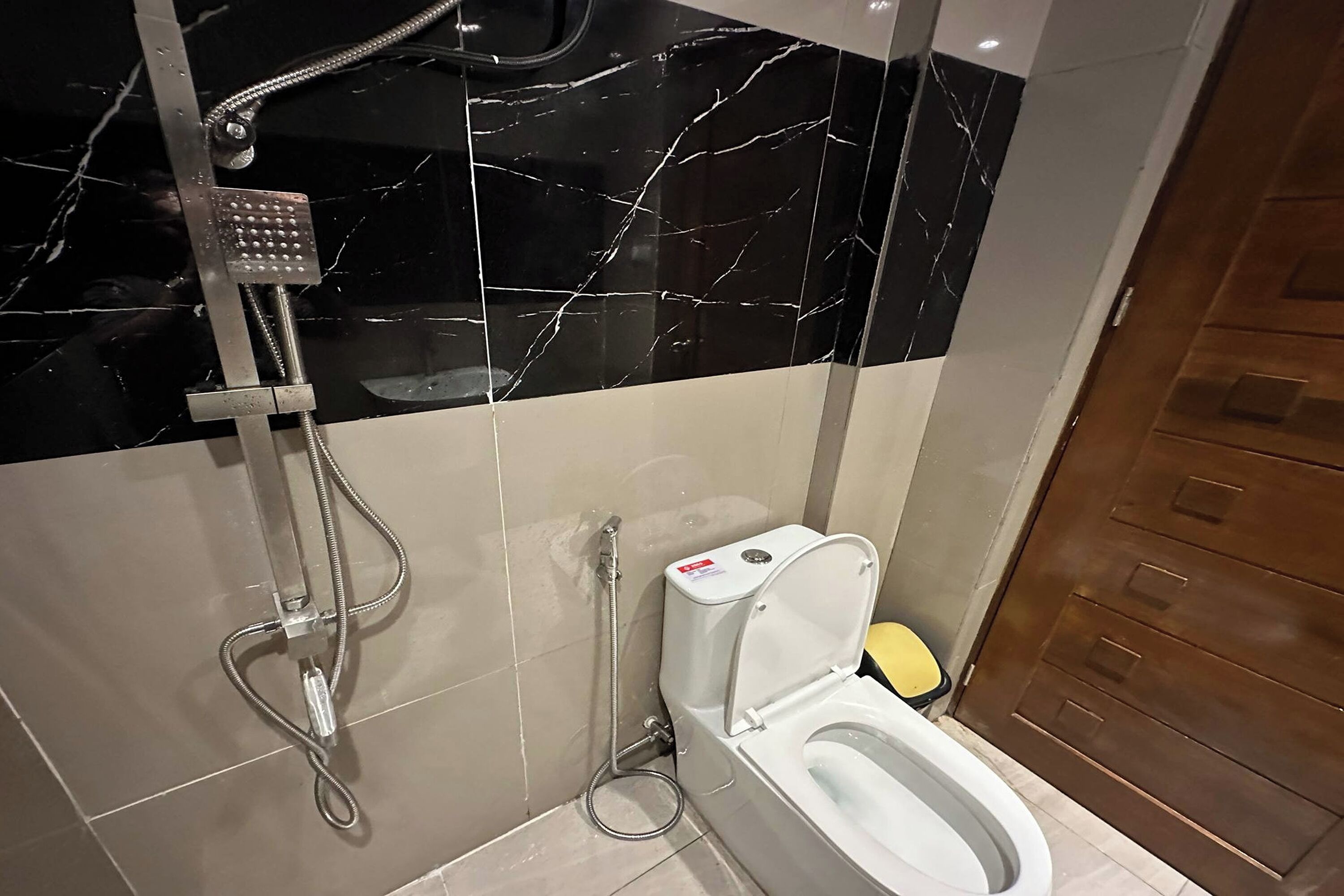 A bathroom with a shower, toilet, and marble-tiled walls.