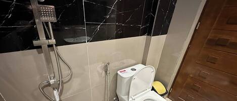 A bathroom with a shower, toilet, and marble-tiled walls.