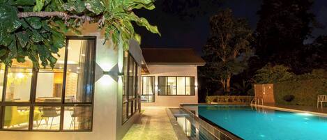 A modern house with a swimming pool, large windows, and a well-lit exterior.