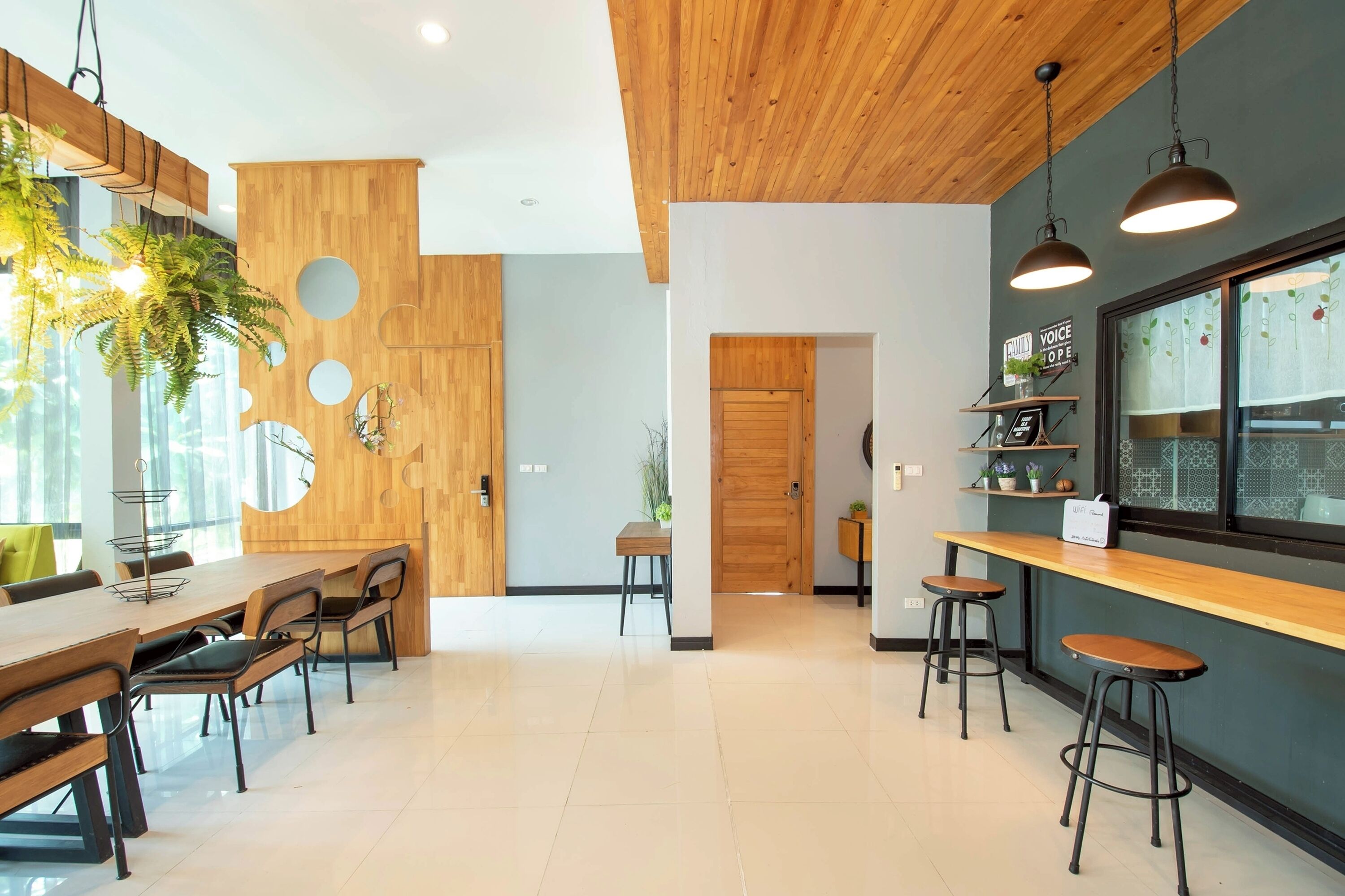 A modern dining area with wooden tables and chairs, a bar counter with stools, and a large window with a view.