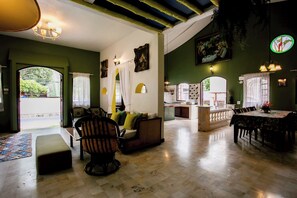 A spacious living area with a sofa, chairs, a dining table, and a kitchen in the background.