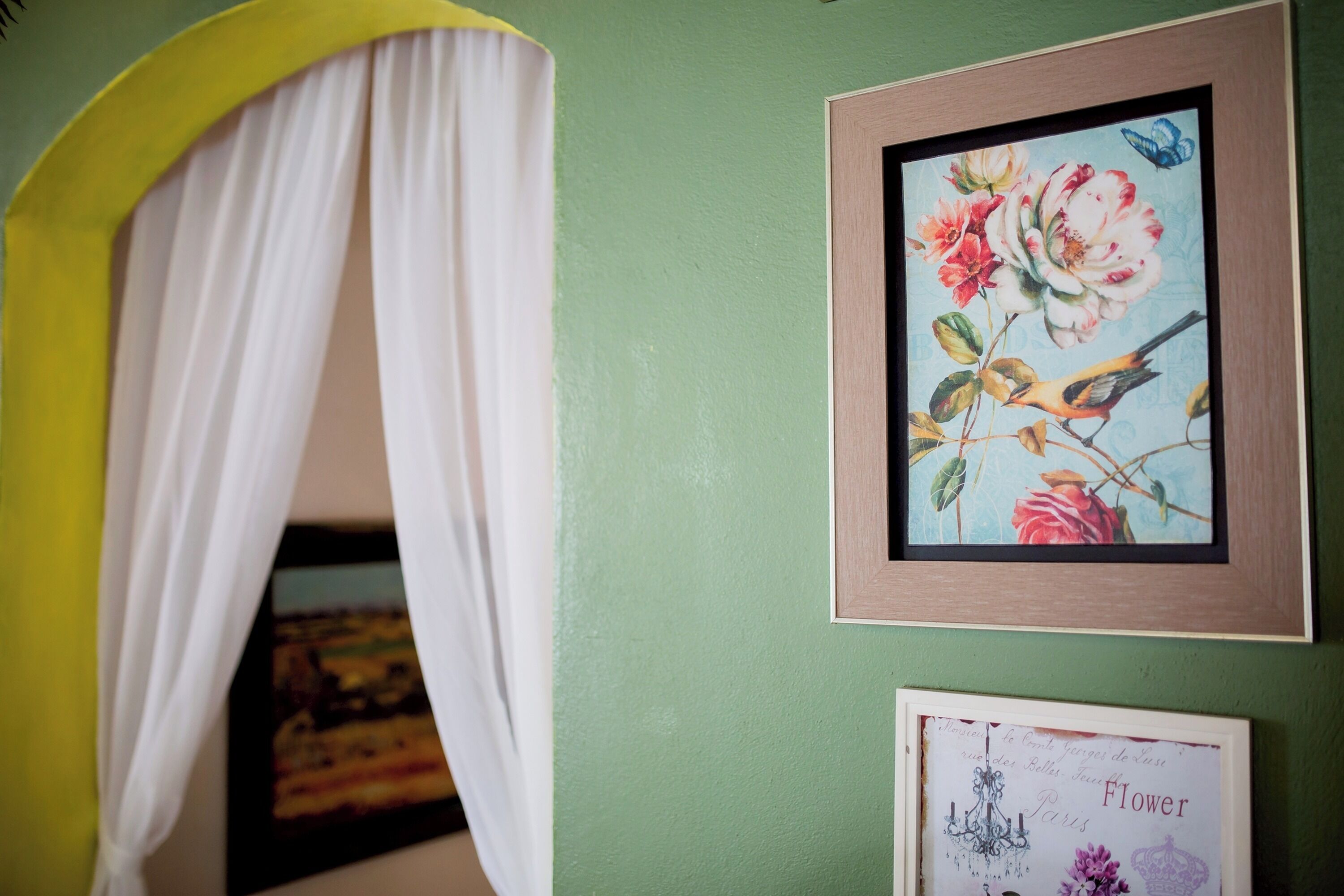 A room with a green wall, a framed floral artwork, and a white curtain.