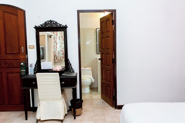 A hotel room with a wooden desk, a chair, a mirror, a toilet, and a bed.