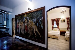A hotel room with a large painting, a chandelier, and a bed with red curtains.