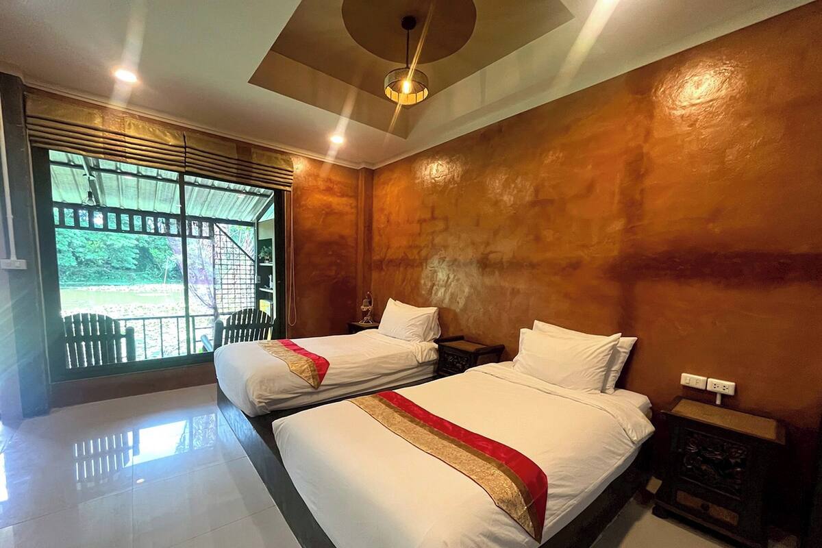 A hotel room with two beds, a large window with a view of greenery, and a ceiling light fixture.