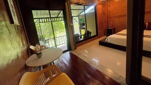 A room with a bed, a small table, and a chair. There is a window with a view of greenery outside. - Saikaew Resort (Chiang Rai)