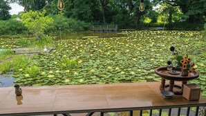 A wooden deck with a table and chairs overlooking a pond with lily pads and water lilies. - Saikaew Resort (Chiang Rai)