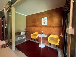 Una stanza con pavimento rosso, due sedie gialle, un tavolo bianco e un quadro appeso al muro.