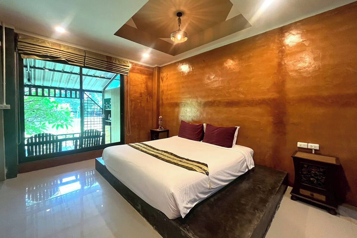 A modern bedroom with a large bed, a ceiling fan, and a view of greenery outside.