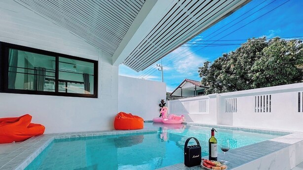 Ein moderner Poolbereich im Freien mit einem klaren blauen Pool, einer Liege, einem rosa Schwimmreifen und einer Weinflasche am Pool.