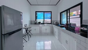 Eine moderne Küche mit weißen Schränken, einem Esstisch mit Stühlen, einem großen Fenster mit Blick und einem Kühlschrank.