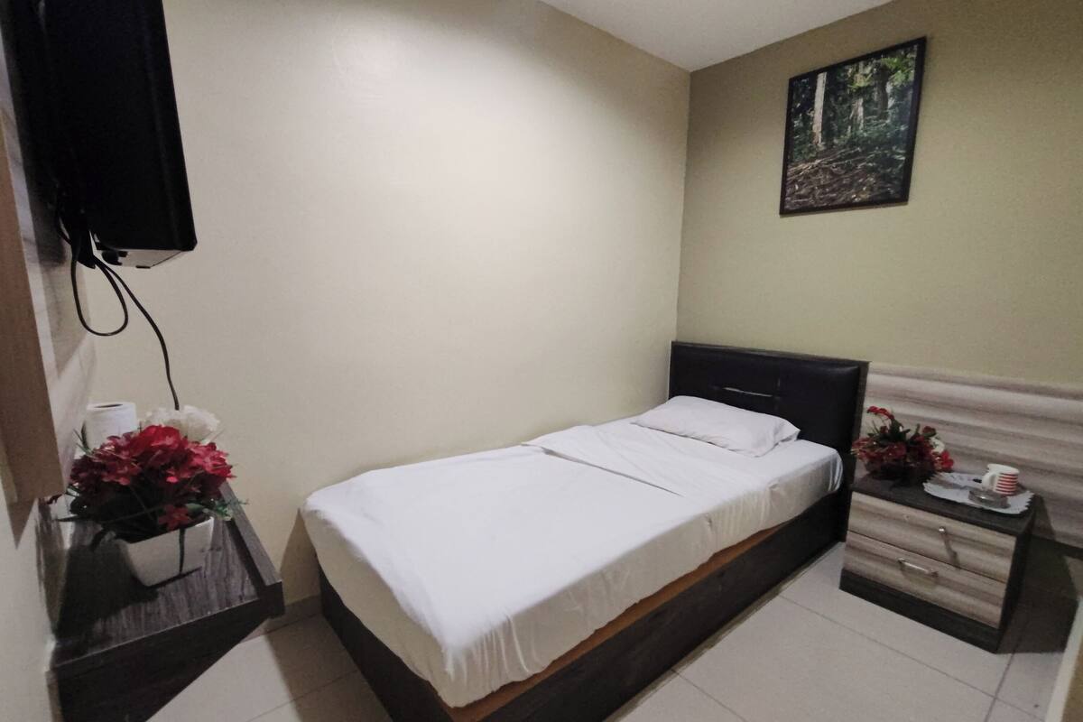 A bedroom with a bed, a nightstand, a wall-mounted TV, a painting, and a flower arrangement.