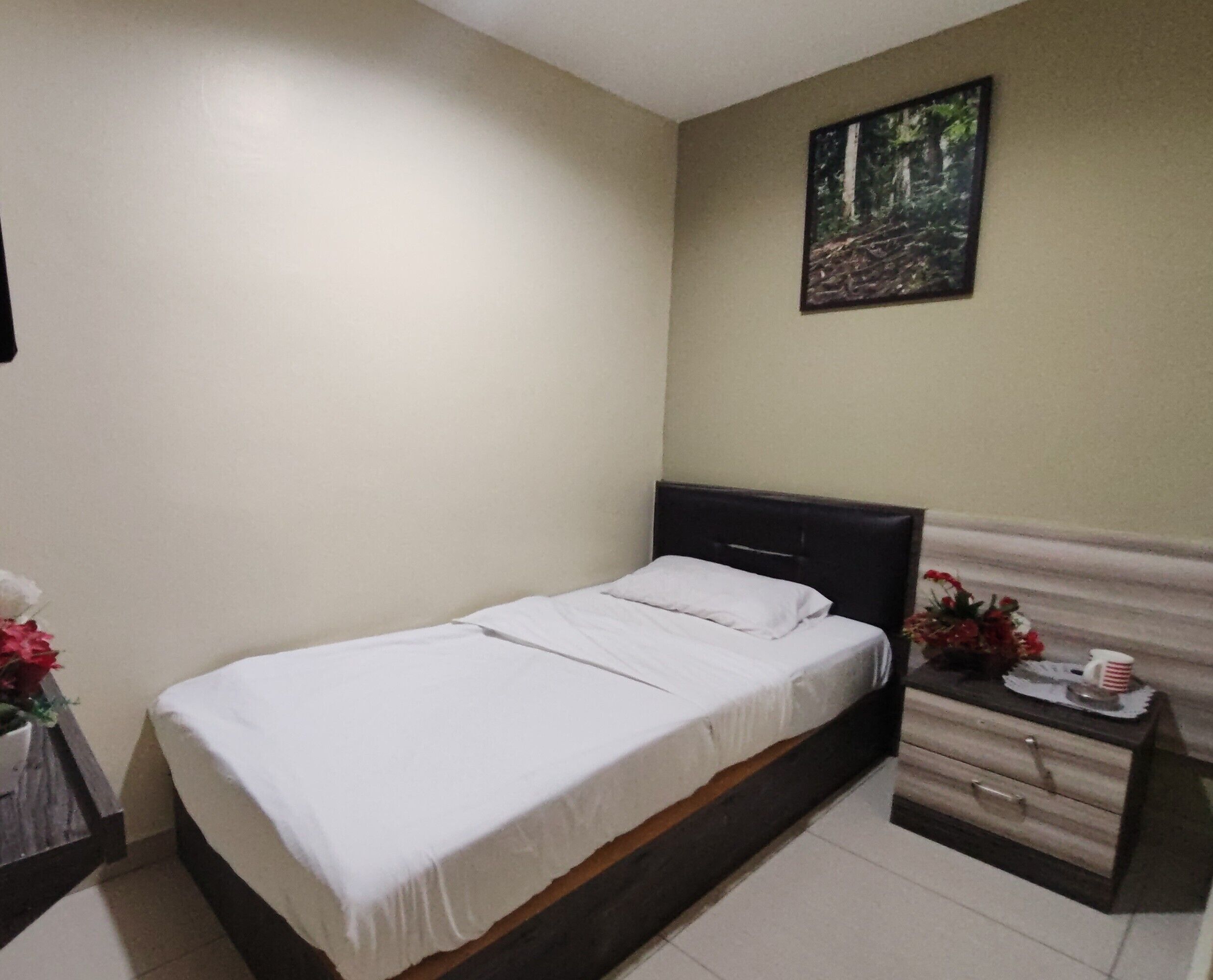 Una cama individual con ropa de cama blanca, un cabecero oscuro y una mesita de noche con cajones y una pequeña mesa.