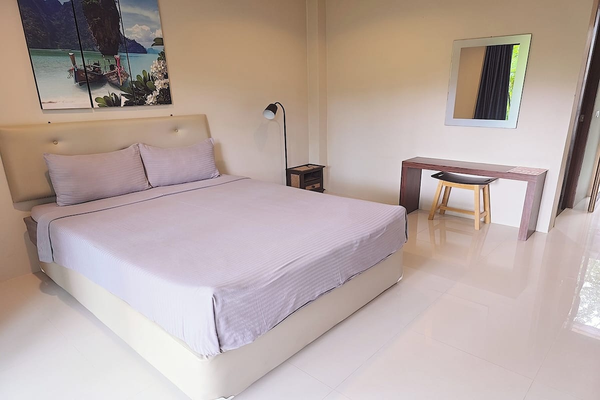 Un dormitorio con una cama, un escritorio, una silla, una mesita de noche, una lámpara, un espejo y un cuadro en la pared.