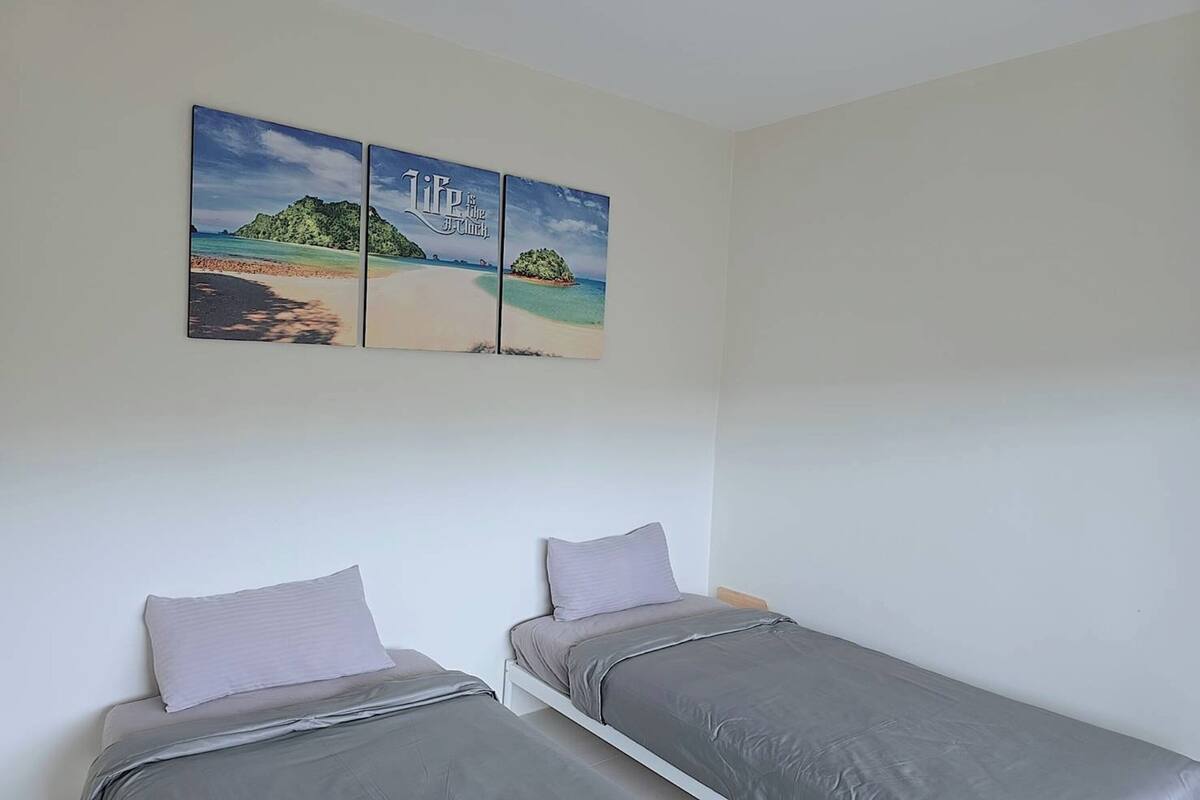 Una habitación con dos camas individuales, una obra de arte colgada en la pared que representa una playa, y una pared blanca lisa.