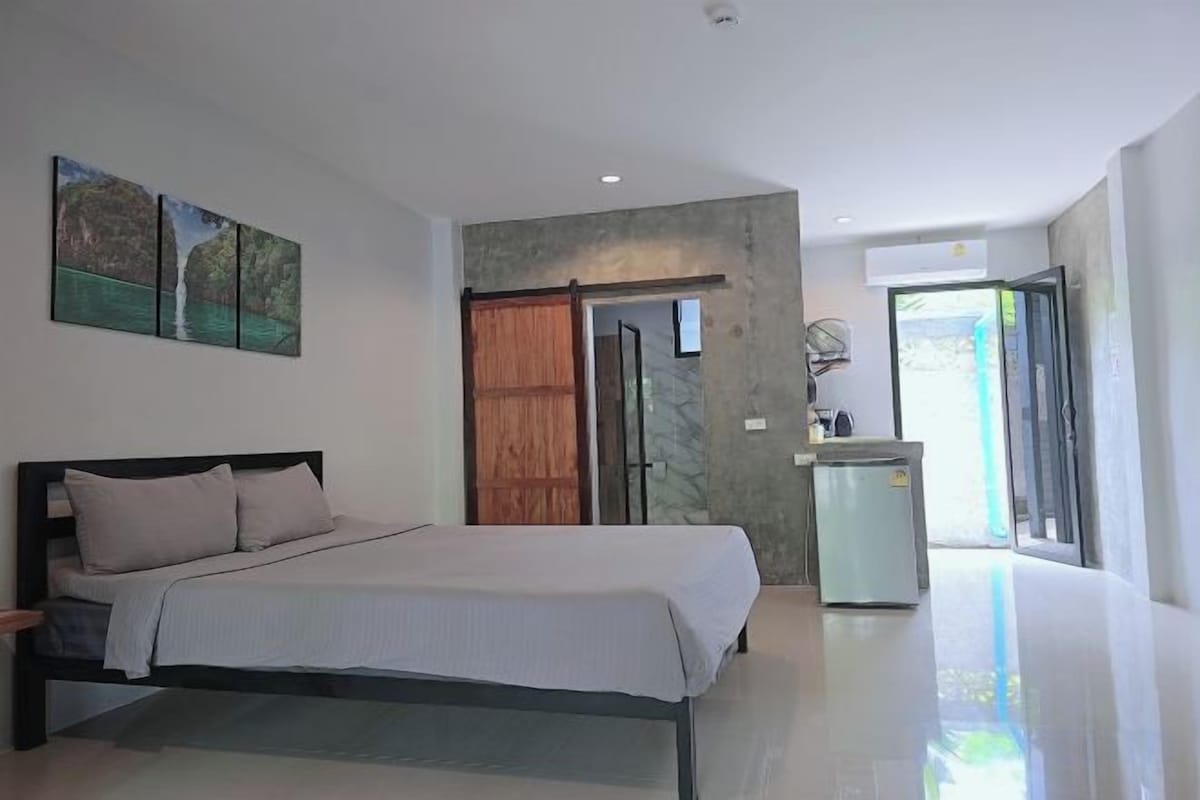 A bedroom with a bed, a wooden door, and a small kitchenette.