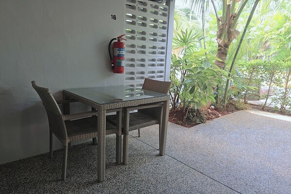 Une table et des chaises en osier sont placées contre un mur, et un extincteur y est fixé.