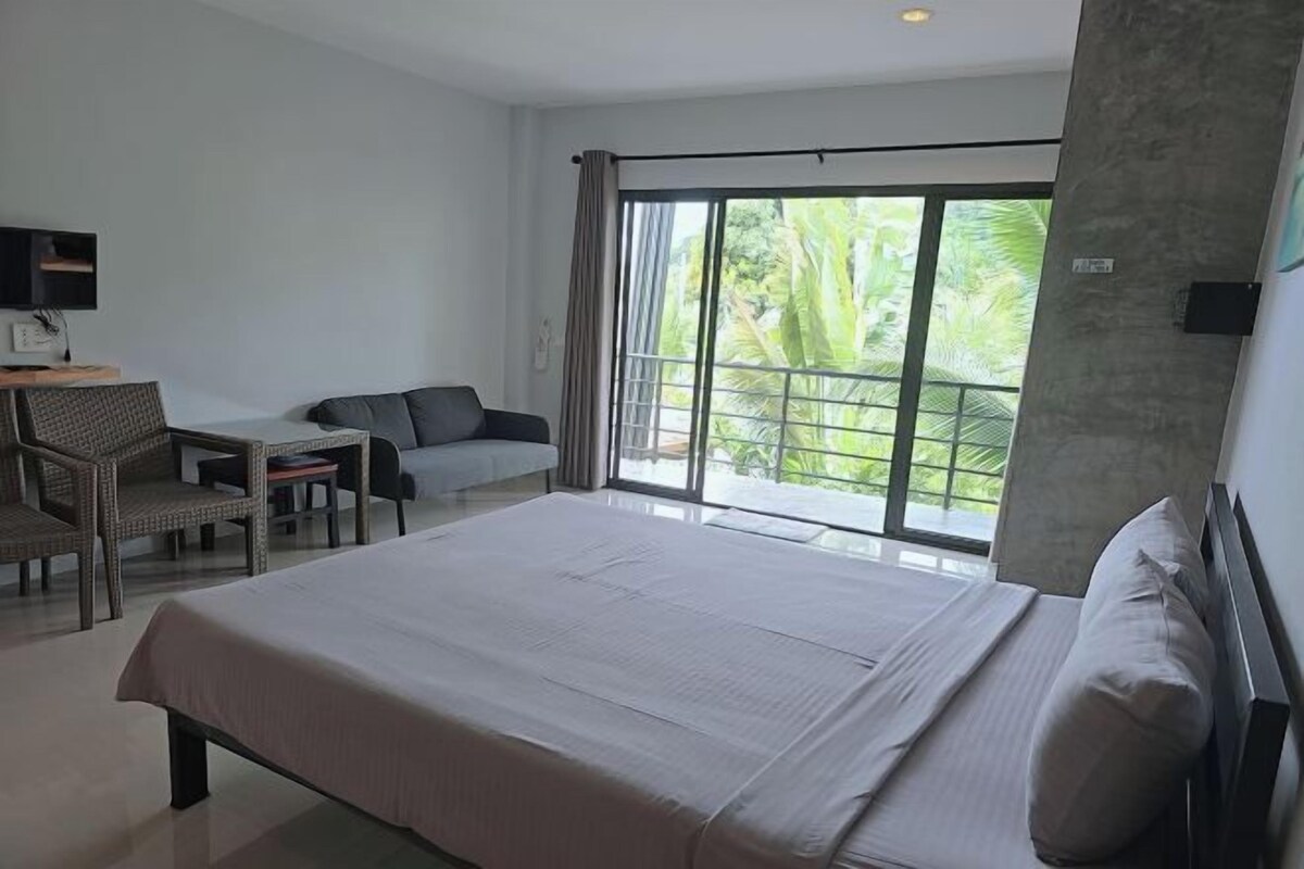 Une chambre d’hôtel avec un grand lit, un bureau avec une chaise, un canapé et un balcon donnant sur un espace verdoyant.