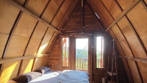 A cozy attic bedroom with a wooden bunk bed, a small table, and a window overlooking a balcony. - Munduk Terrace (Munduk)
