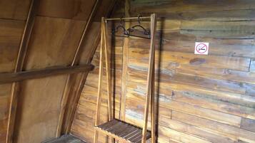 A wooden loft bedroom with a sloped ceiling and a wooden bench with hooks.