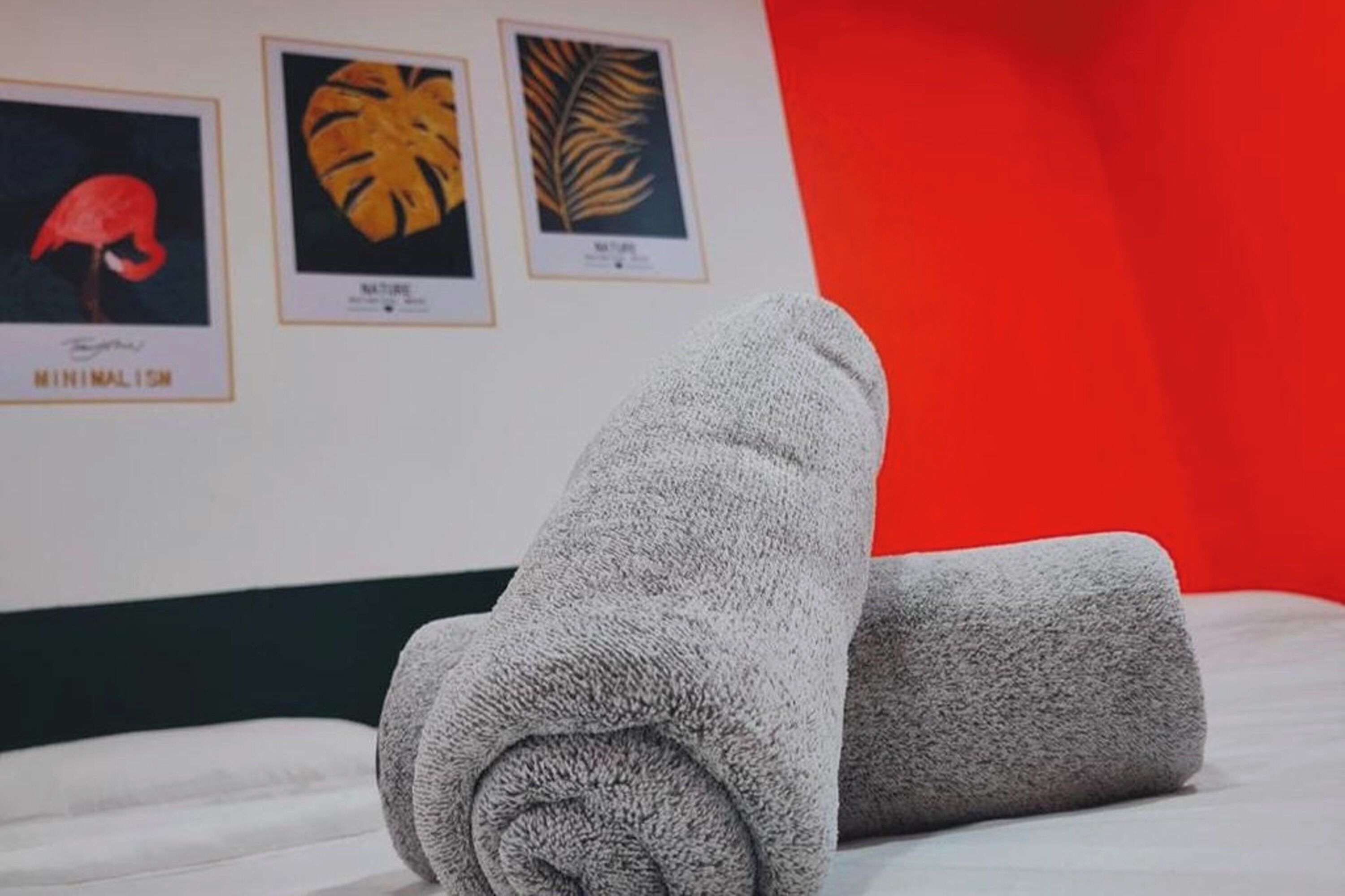 A neatly made bed with two rolled-up towels and framed botanical prints on the wall.