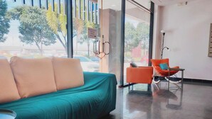 A modern hotel lobby with a teal sofa, orange chairs, and a glass partition.